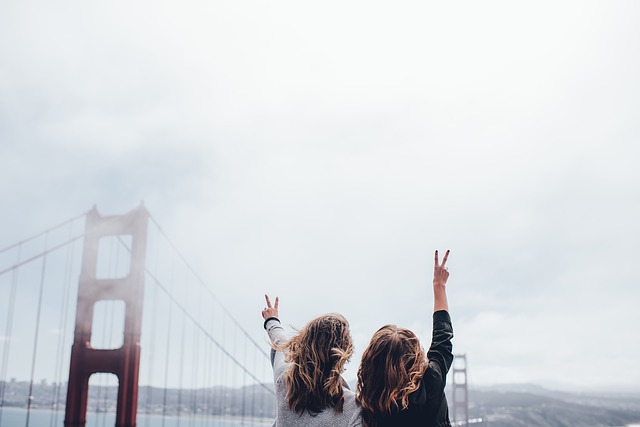 Two People Making Peace Signs With The Golden Gate Bridge In The Background